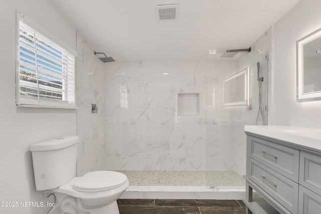 full bath with toilet, a marble finish shower, visible vents, and vanity