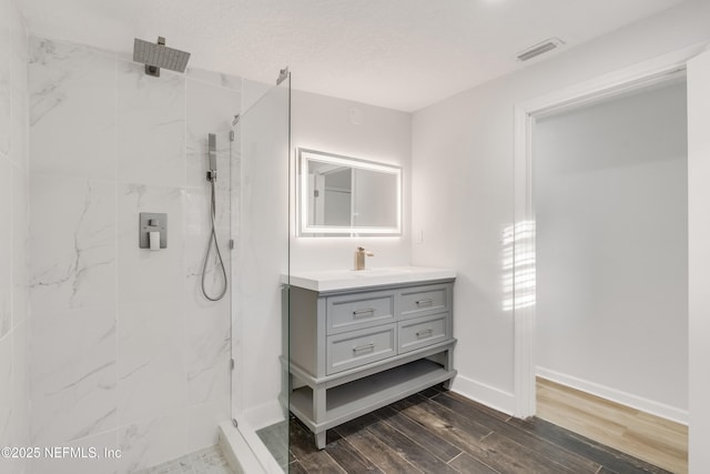 bathroom featuring baseboards, vanity, a marble finish shower, and wood finished floors