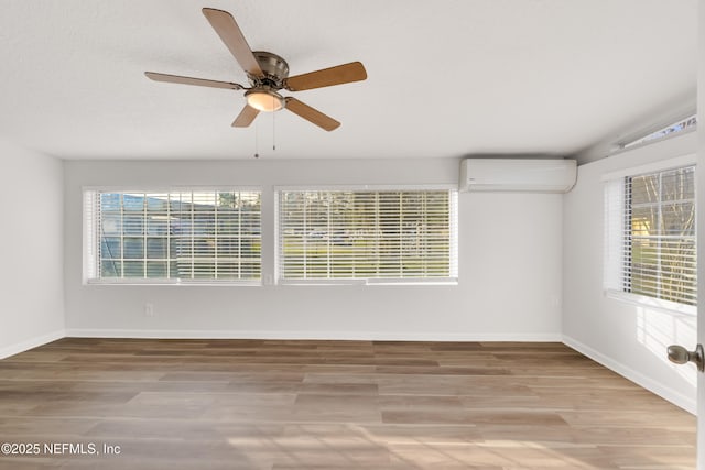 empty room featuring a wall mounted air conditioner, plenty of natural light, baseboards, and wood finished floors