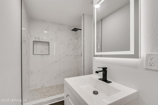 bathroom with a textured wall, a marble finish shower, and vanity