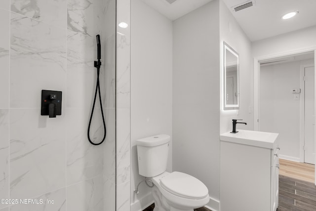 full bath with a marble finish shower, visible vents, toilet, vanity, and wood finished floors