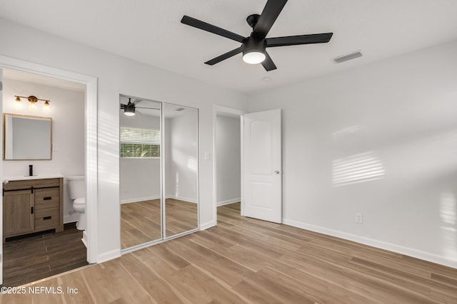 unfurnished bedroom featuring visible vents, light wood-style flooring, a sink, ensuite bath, and baseboards