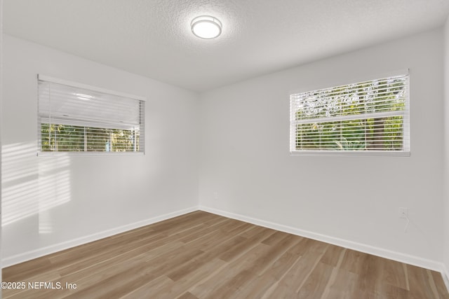 empty room with a textured ceiling, plenty of natural light, wood finished floors, and baseboards