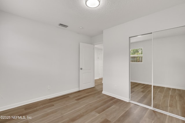 unfurnished bedroom with a closet, visible vents, a textured ceiling, wood finished floors, and baseboards