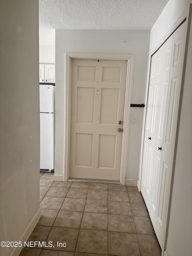 hallway with a textured ceiling, baseboards, and light tile patterned floors