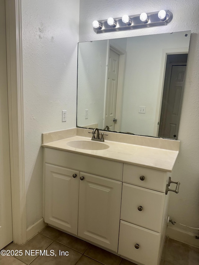 bathroom with a textured wall, tile patterned flooring, vanity, and baseboards