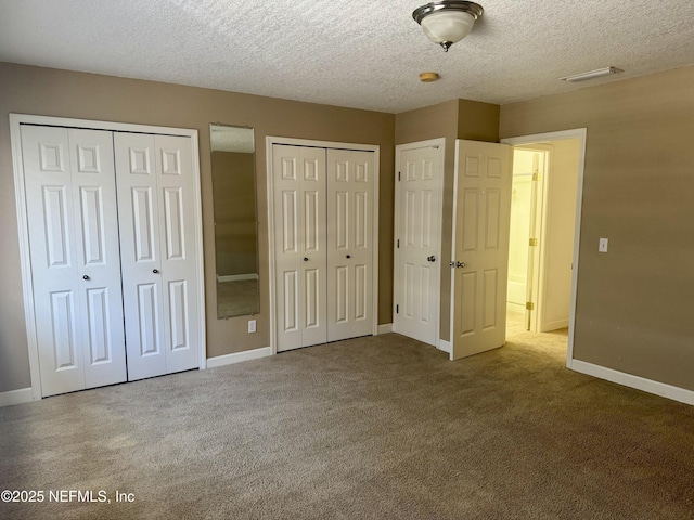 unfurnished bedroom featuring a textured ceiling, carpet flooring, visible vents, baseboards, and multiple closets