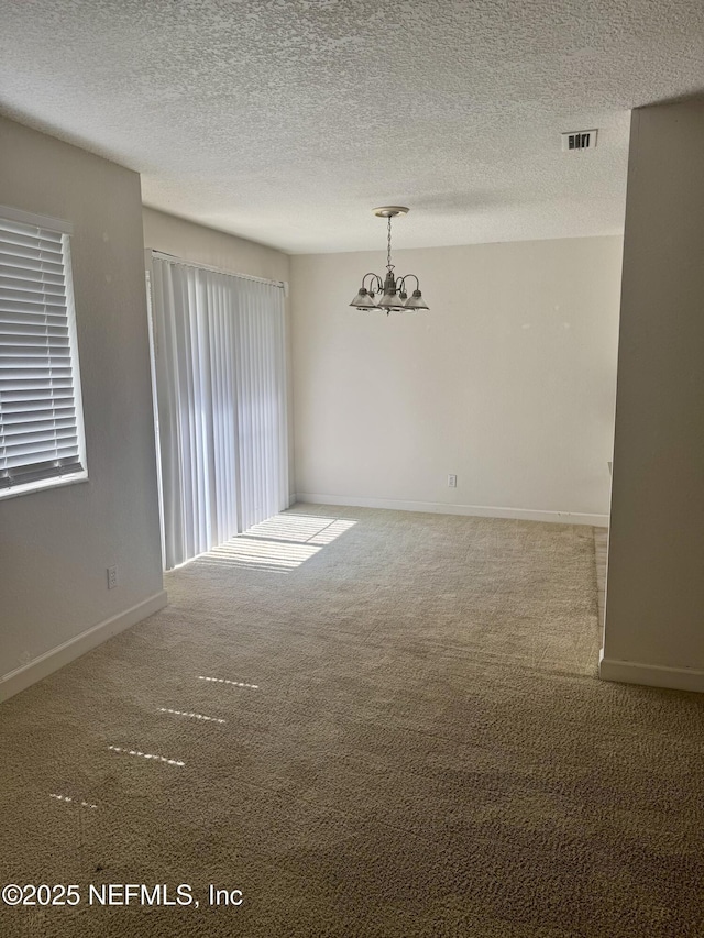 spare room with visible vents, an inviting chandelier, carpet flooring, a textured ceiling, and baseboards