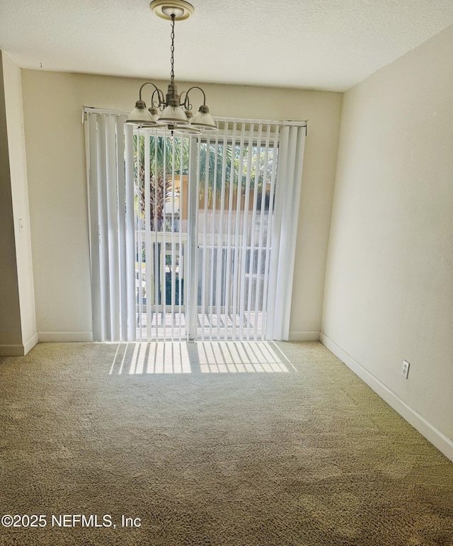 unfurnished dining area with carpet floors, a textured ceiling, baseboards, and an inviting chandelier