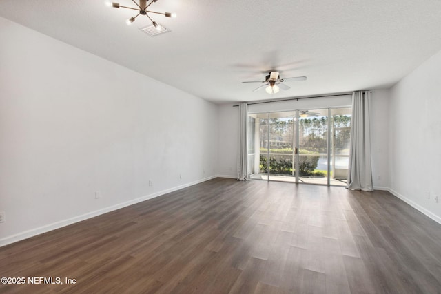 empty room featuring ceiling fan with notable chandelier, dark wood-type flooring, and baseboards