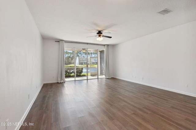 spare room with ceiling fan, visible vents, dark wood finished floors, and baseboards