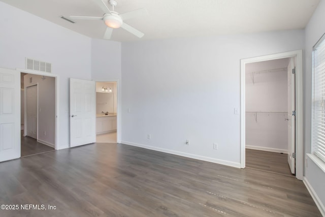 unfurnished bedroom with a walk in closet, visible vents, baseboards, and wood finished floors