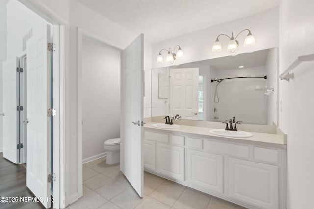 bathroom with double vanity, a sink, toilet, and tile patterned floors