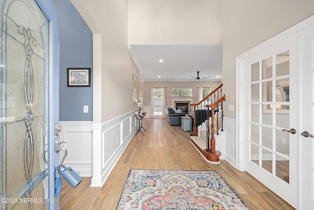 entryway featuring light wood finished floors, a wainscoted wall, a fireplace, and arched walkways