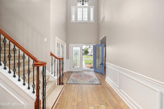 foyer entrance with stairway, light wood finished floors, arched walkways, wainscoting, and a decorative wall