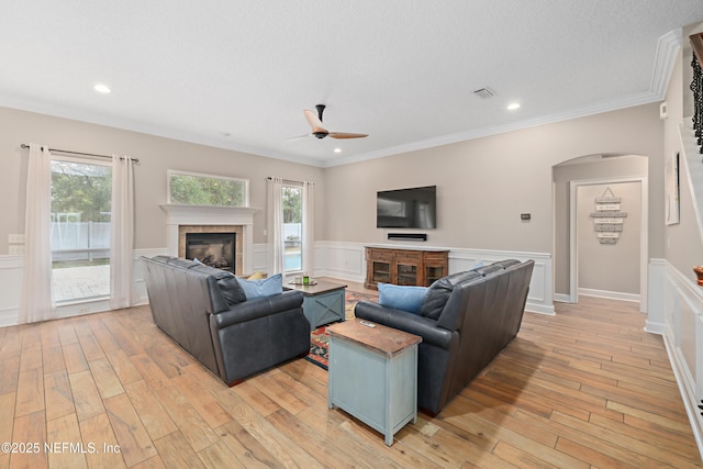 living area featuring a tiled fireplace, arched walkways, visible vents, and light wood-type flooring