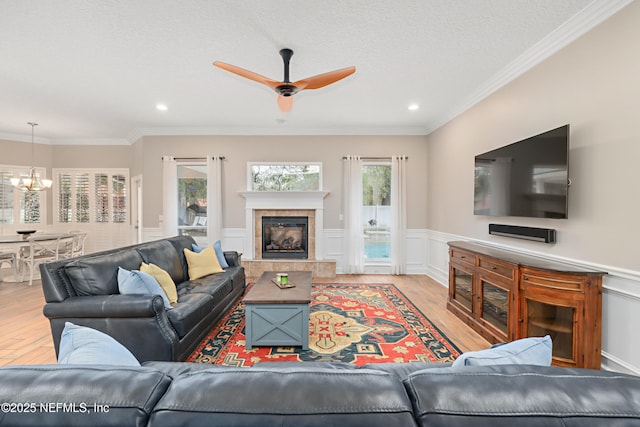 living area with ceiling fan with notable chandelier, wood finished floors, wainscoting, a fireplace, and crown molding