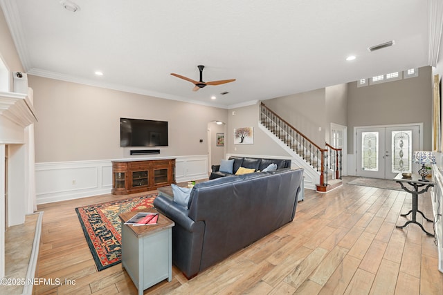 living area featuring stairway, a wainscoted wall, french doors, crown molding, and light wood-type flooring