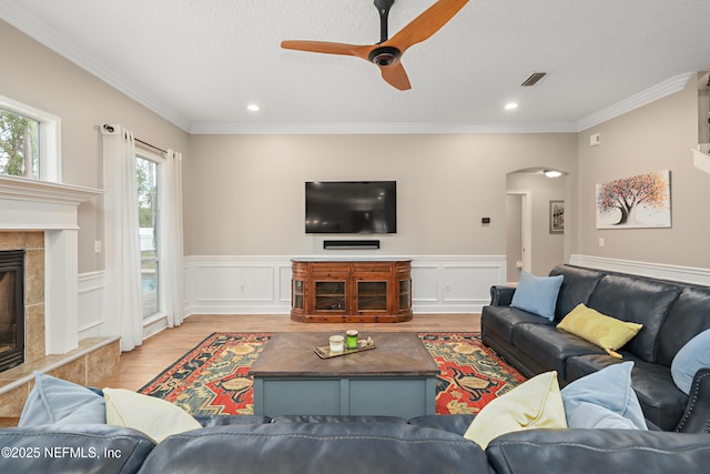 living area with visible vents, a fireplace, arched walkways, light wood-style floors, and crown molding