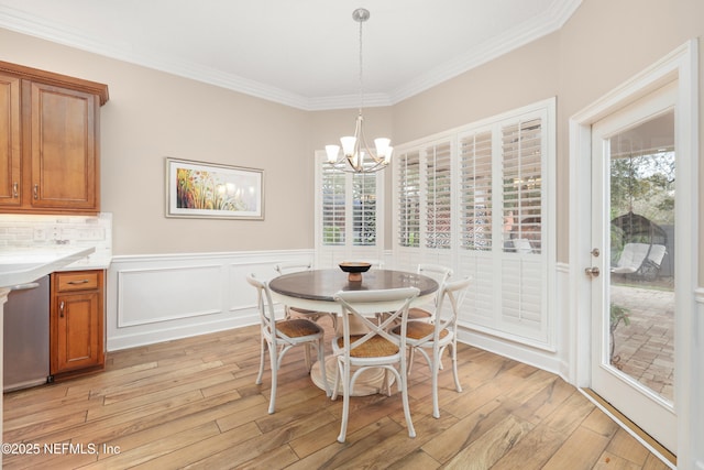 dining space featuring a wainscoted wall, ornamental molding, an inviting chandelier, light wood-style floors, and a decorative wall