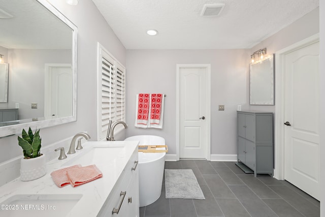 full bathroom with baseboards, double vanity, a freestanding tub, tile patterned floors, and a sink