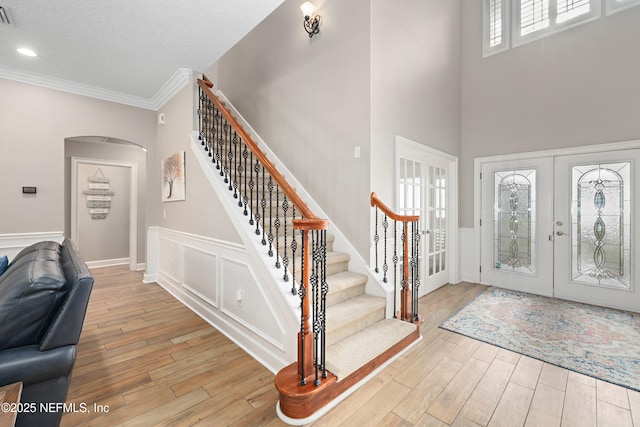 entrance foyer featuring wood finished floors, french doors, arched walkways, crown molding, and stairs