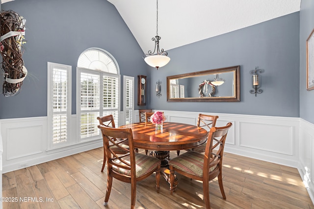 dining room featuring light wood-type flooring, lofted ceiling, and a wainscoted wall