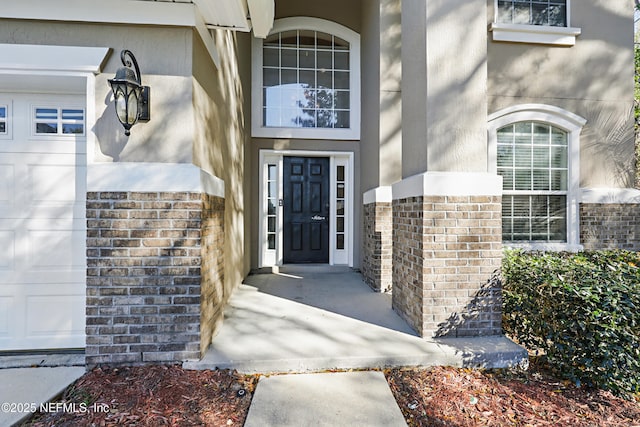 entrance to property with a garage, brick siding, and stucco siding