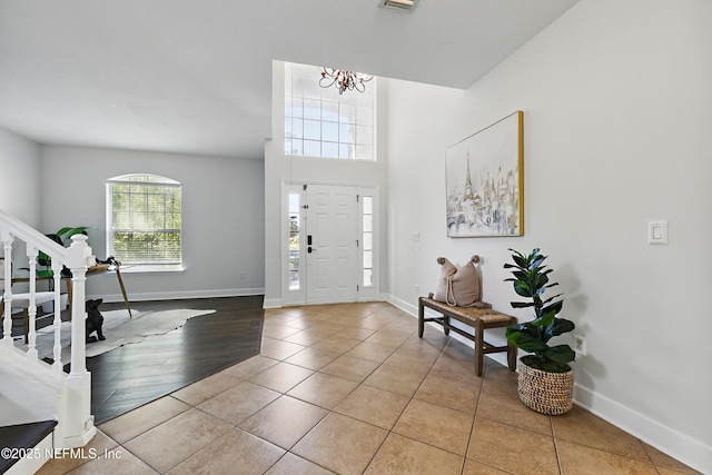 tiled foyer featuring stairs, a chandelier, and baseboards