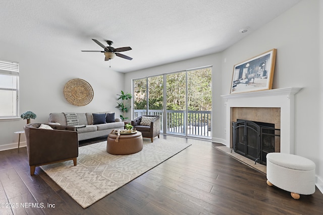 living area with a textured ceiling, a fireplace, a ceiling fan, and dark wood-style flooring