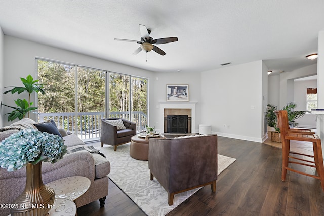 living room featuring a tiled fireplace, dark wood finished floors, visible vents, and a ceiling fan