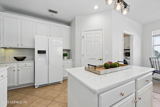 kitchen with light tile patterned flooring, visible vents, white cabinets, a center island, and white fridge with ice dispenser