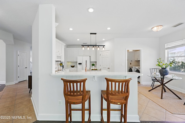 kitchen featuring a peninsula, separate washer and dryer, white appliances, visible vents, and light countertops