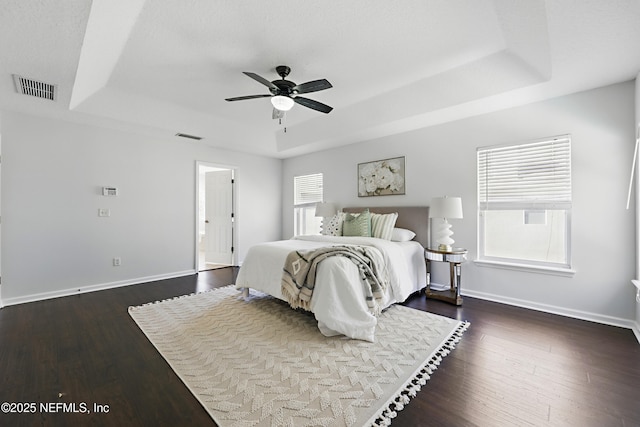 bedroom with dark wood-type flooring, a raised ceiling, multiple windows, and visible vents