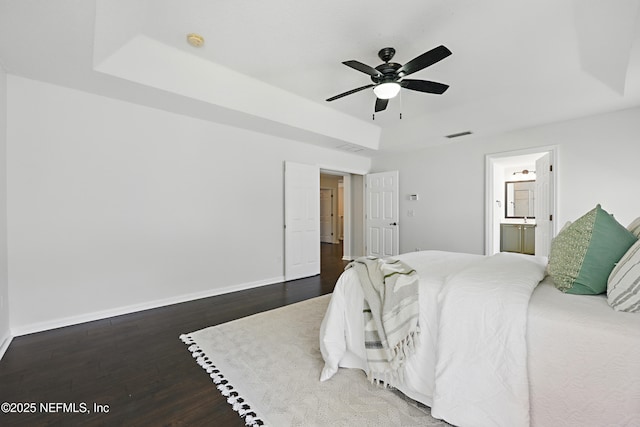 bedroom featuring visible vents, baseboards, a raised ceiling, wood finished floors, and ensuite bathroom