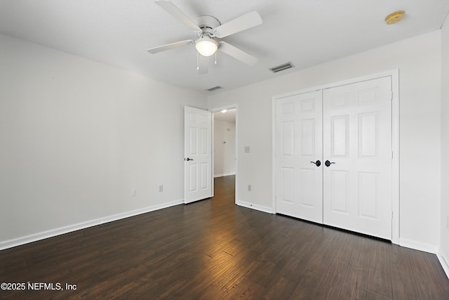 unfurnished bedroom with dark wood-style flooring, a ceiling fan, visible vents, baseboards, and a closet