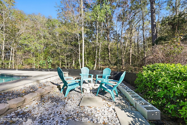 view of patio with an outdoor pool, a fire pit, and a wooded view