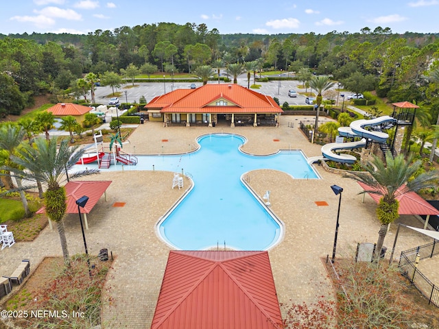 community pool with a water slide, a patio area, and fence