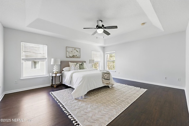 bedroom with dark wood-style floors, baseboards, a tray ceiling, and ceiling fan