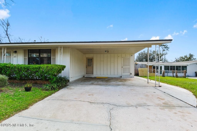 view of front of property with concrete driveway, board and batten siding, a sunroom, an attached carport, and a front lawn