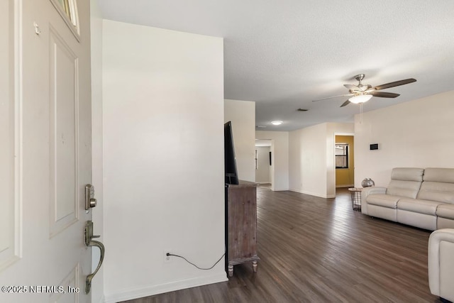 living room with a textured ceiling, dark wood-style flooring, a ceiling fan, and baseboards