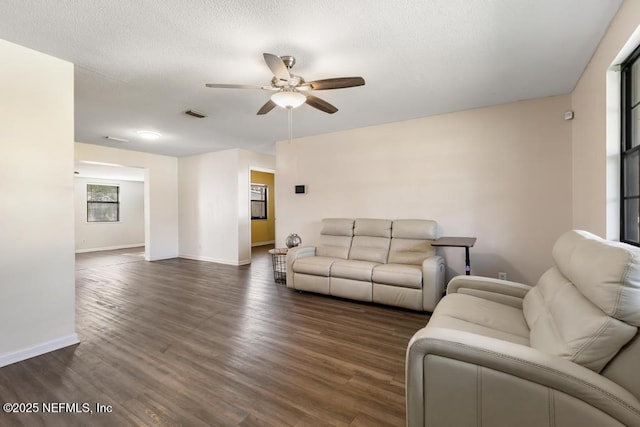 living room with a textured ceiling, visible vents, baseboards, a ceiling fan, and dark wood finished floors