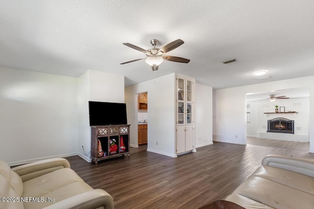 living area with a textured ceiling, a fireplace, visible vents, and dark wood-style flooring