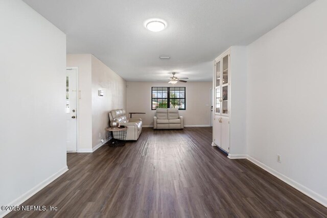 unfurnished room with dark wood finished floors, a ceiling fan, and baseboards