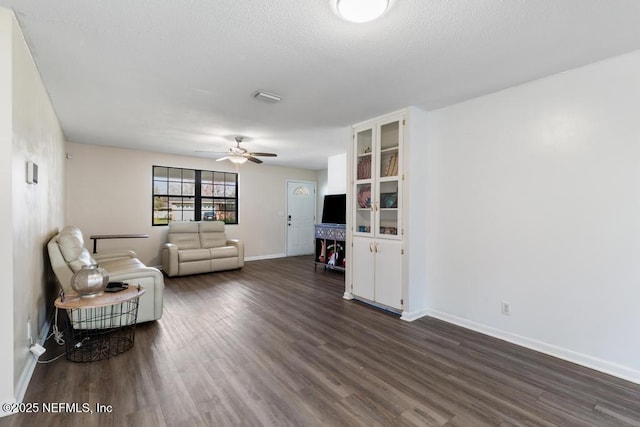 living area with baseboards, visible vents, ceiling fan, dark wood-style flooring, and a textured ceiling