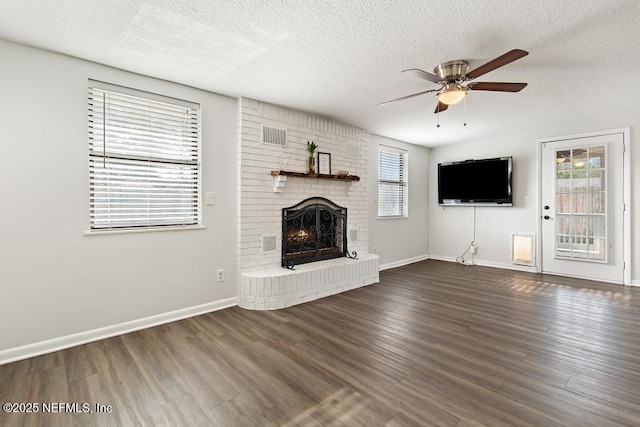 unfurnished living room featuring a brick fireplace, a textured ceiling, baseboards, and wood finished floors