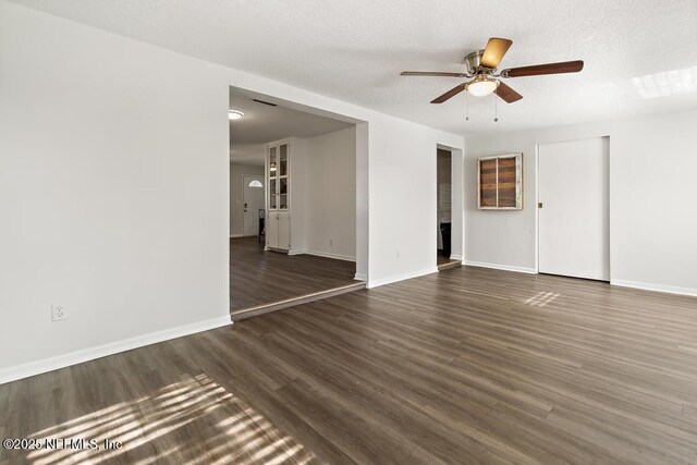 empty room featuring a ceiling fan, a textured ceiling, baseboards, and dark wood-type flooring