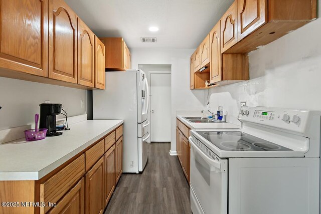 kitchen with light countertops, visible vents, dark wood-type flooring, a sink, and white appliances