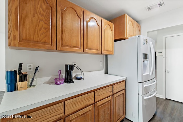 kitchen featuring dark wood-style floors, light countertops, white fridge with ice dispenser, and visible vents