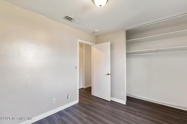 unfurnished bedroom with a textured ceiling, visible vents, baseboards, a closet, and dark wood-style floors